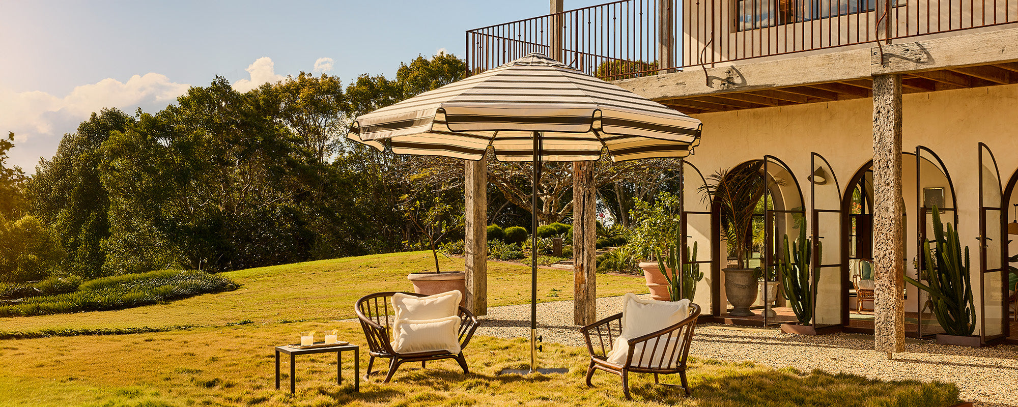Basil Bangs commercial and residential black frame patio umbrella with black Al Mare stripe canopy. Outdoor cushion covers in Ecru, neutral with fringe.