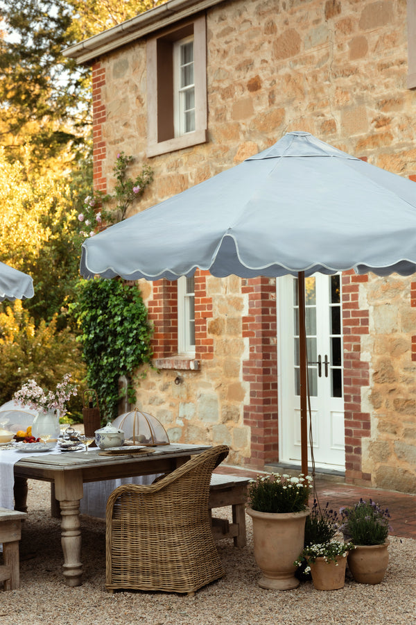 Basil Bangs Dusk Blue Patio umbrella with soft scallop valance against heritage brick house