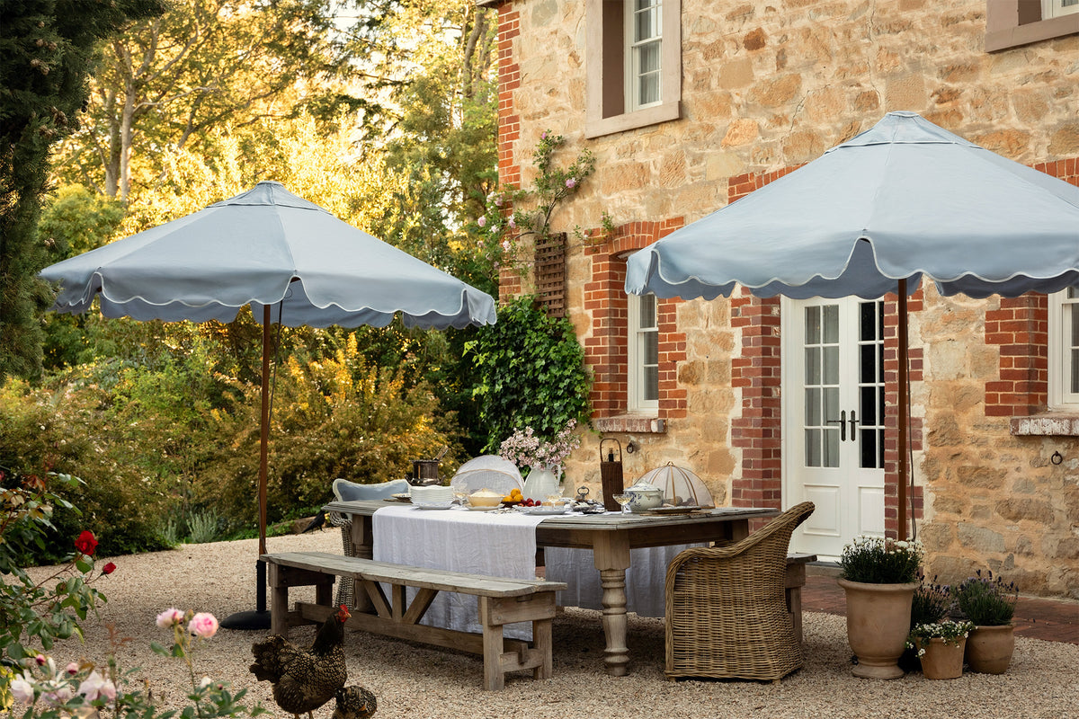 French Provincial looking outdoor dining area with Basil Bangs baby blue patio umbrellas in front of a brick building.