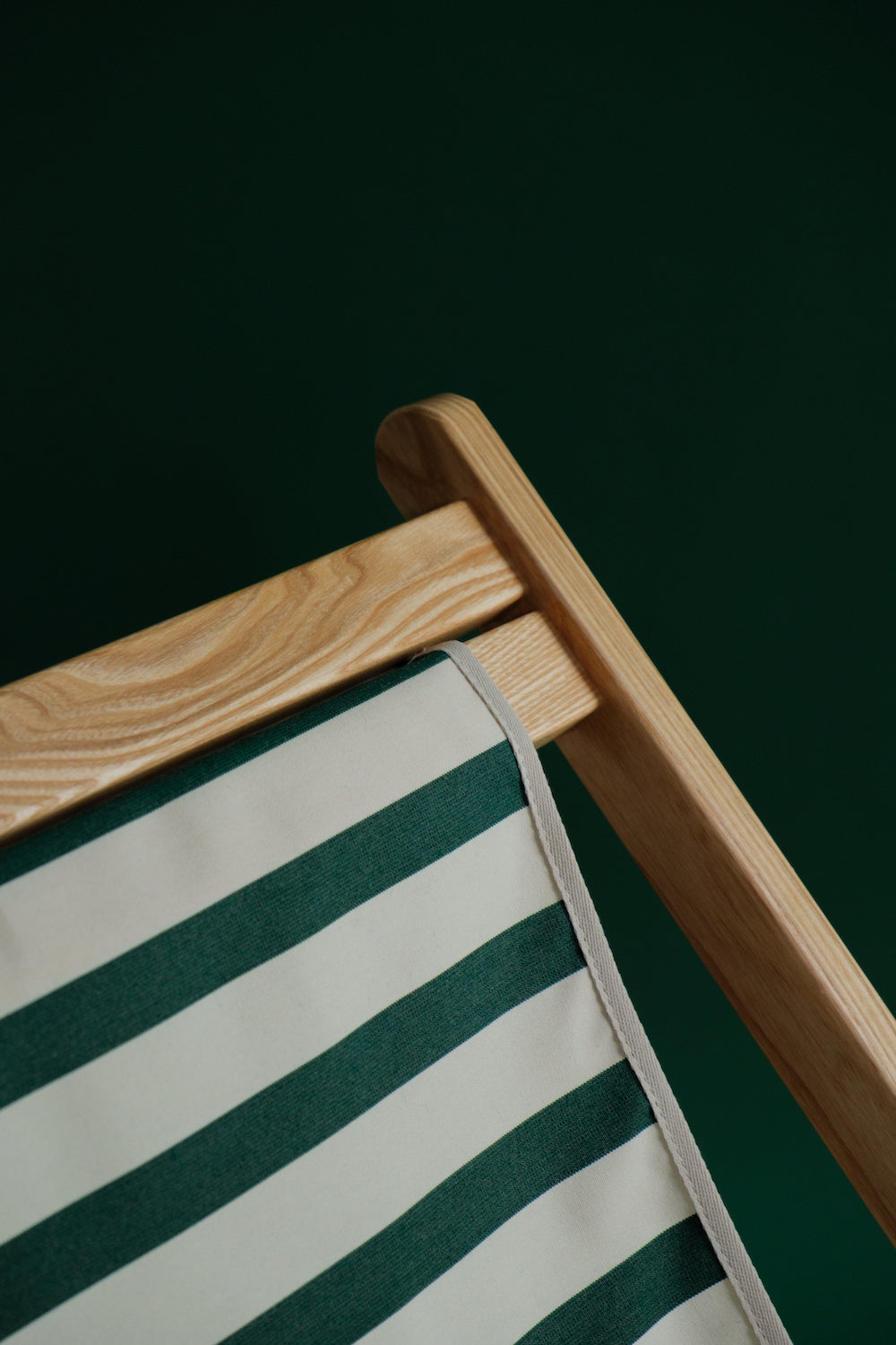 Dark green and white stripe timber deck chair on green background