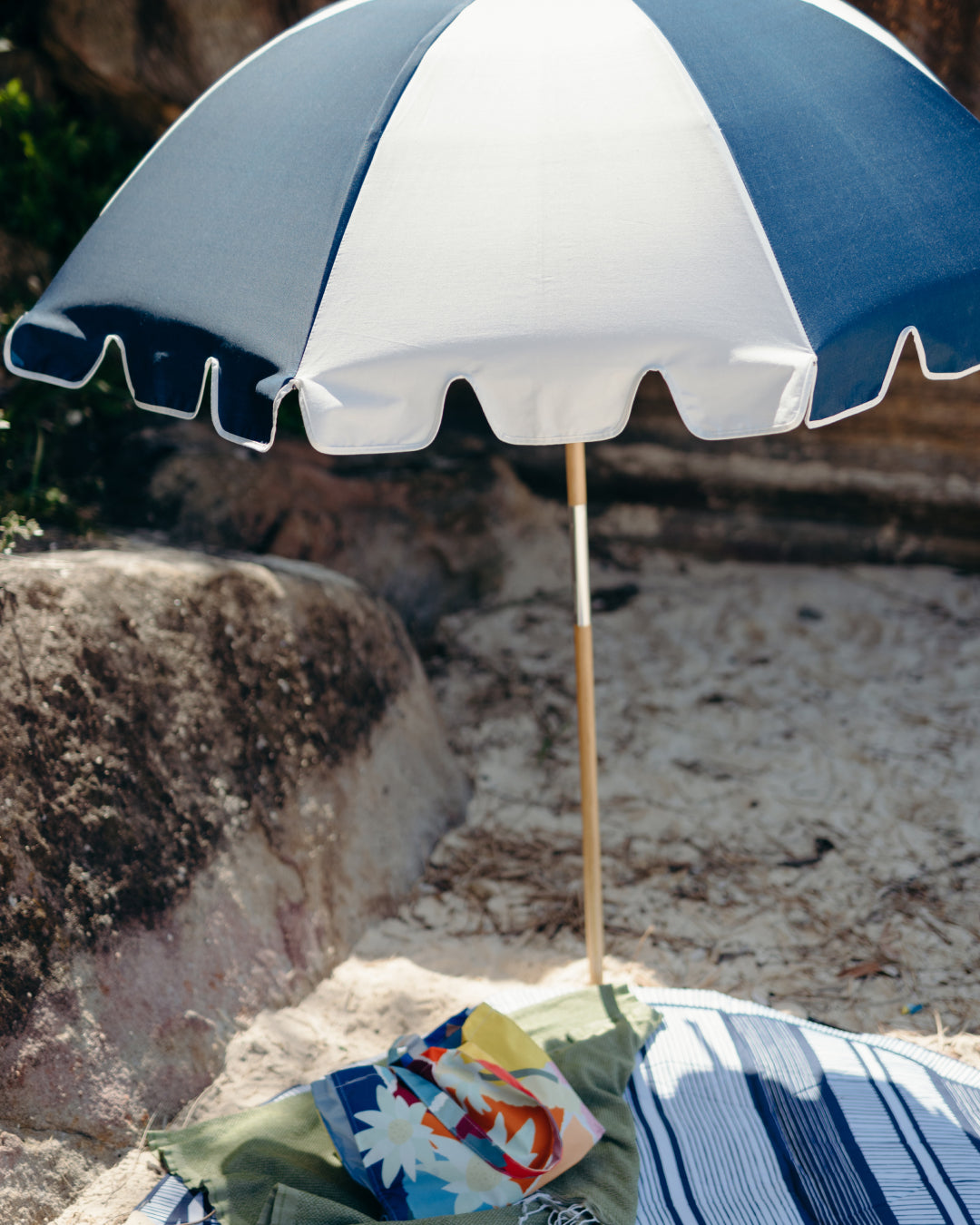 Basil Bangs Steel Blue and white beach umbrella on a sandy surface with a colourful towel underneath.
