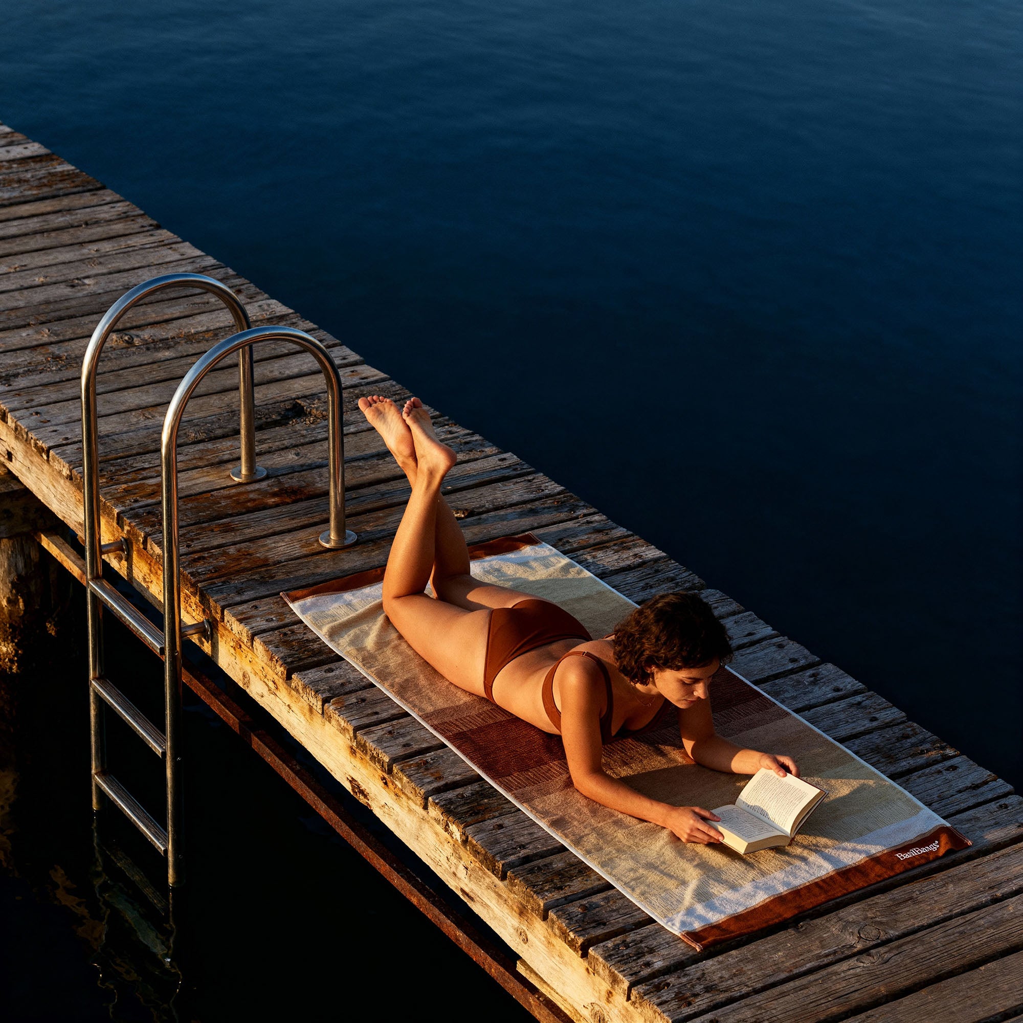 Woman reading a book on a luxury cotton beach towel in Ombre Terra, featuring soft gradient hues and plush texture, perfect for beach days and poolside lounging. 